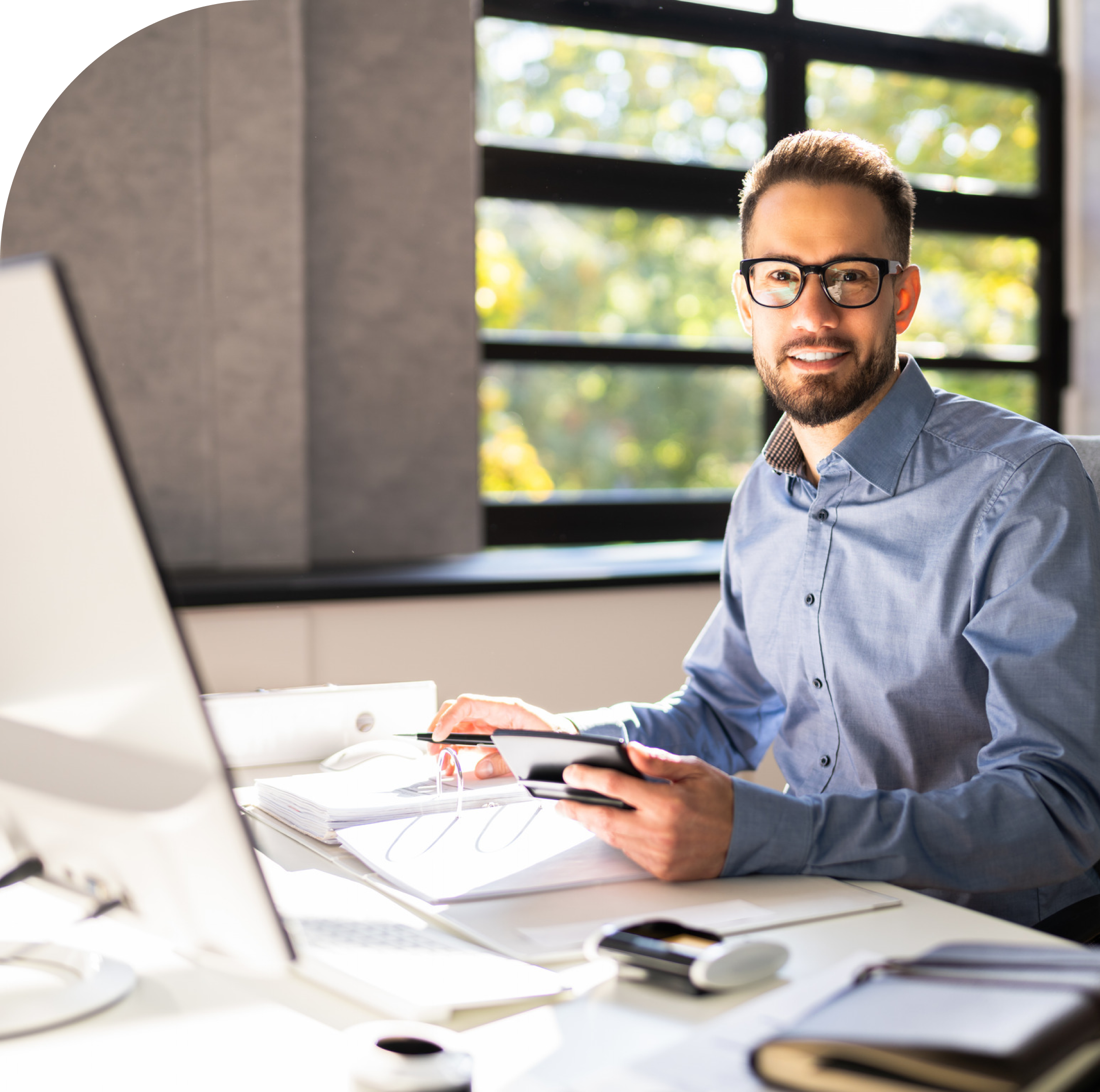 An accountant smiling while sitting at a desk in a sun filled room, representing the war customer service offered by Dynamic Assurance Services PLC.